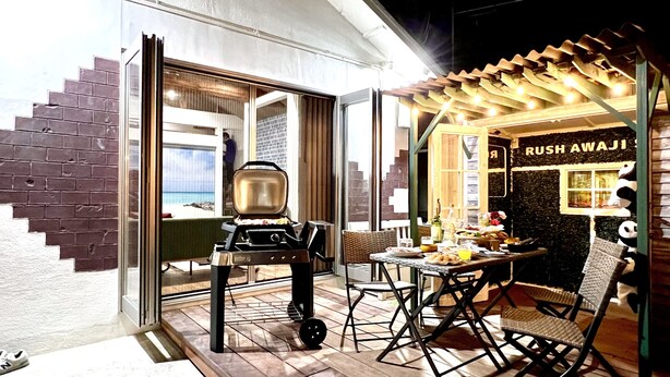 Un espace extérieur aménagé pour les repas, avec un barbecue, des chaises et une table dressée.