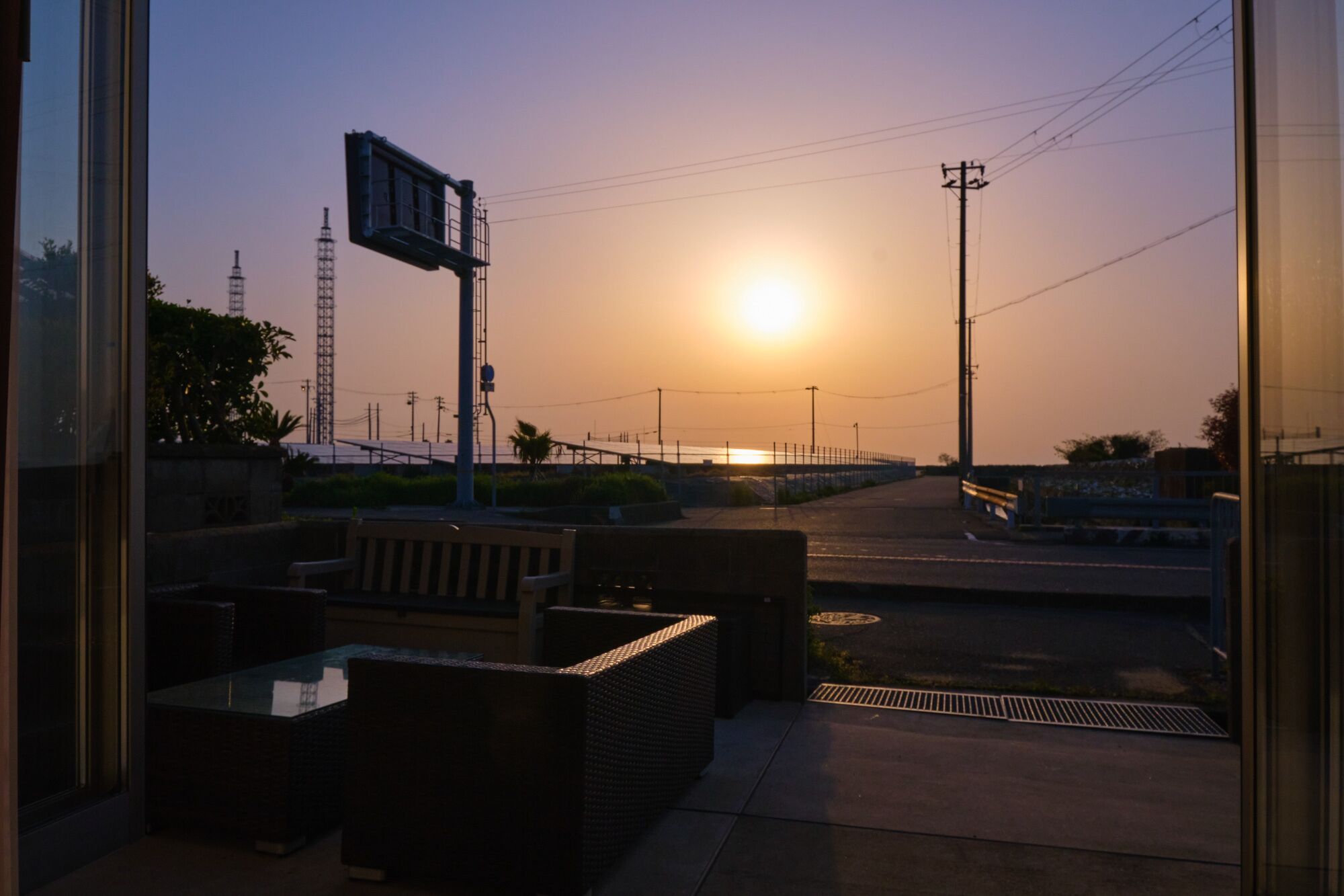 A sunset view from a balcony with outdoor seating and a street in the background.