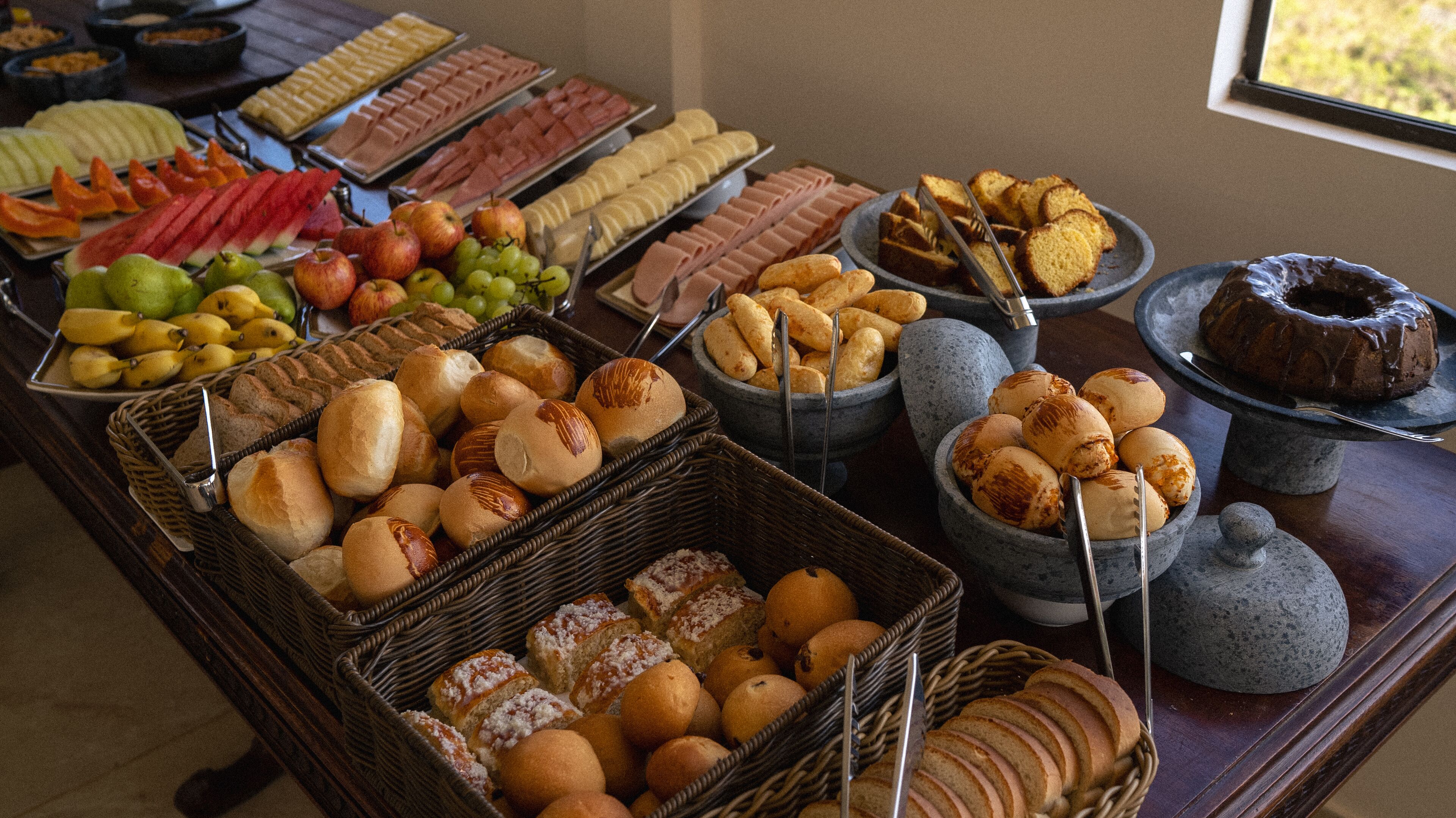 Un bufé con diferentes opciones de comida, incluyendo frutas, pasteles y pan.