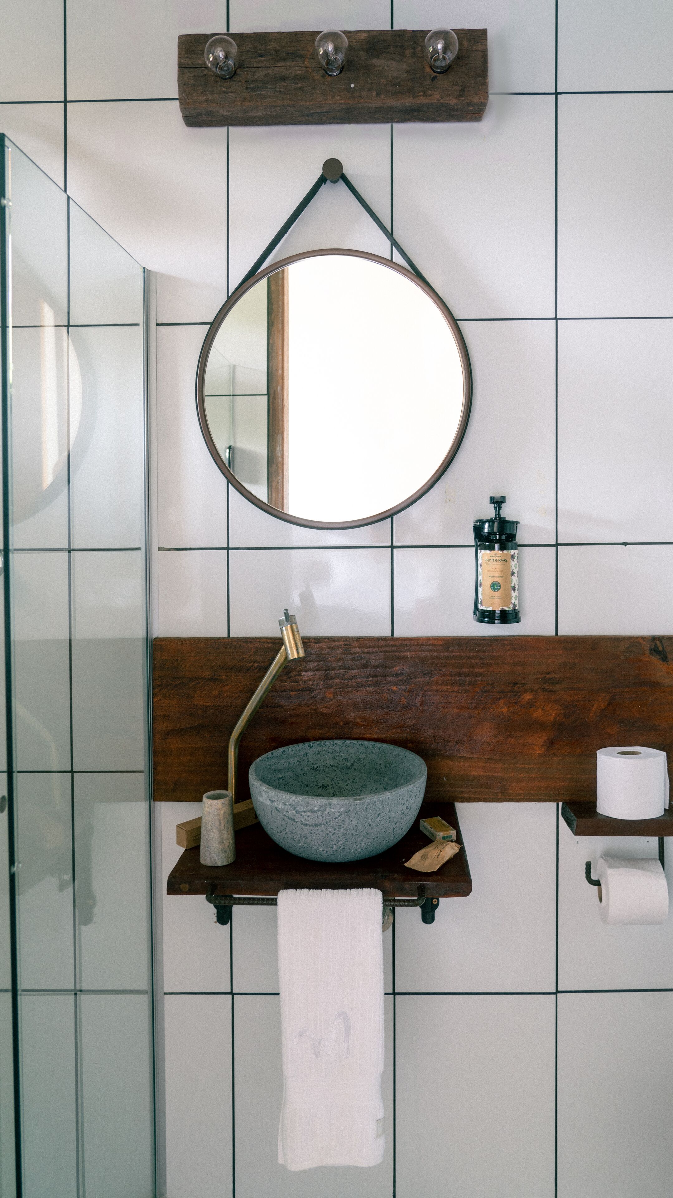 A bathroom with a round mirror, wooden vanity, and a glass shower enclosure.