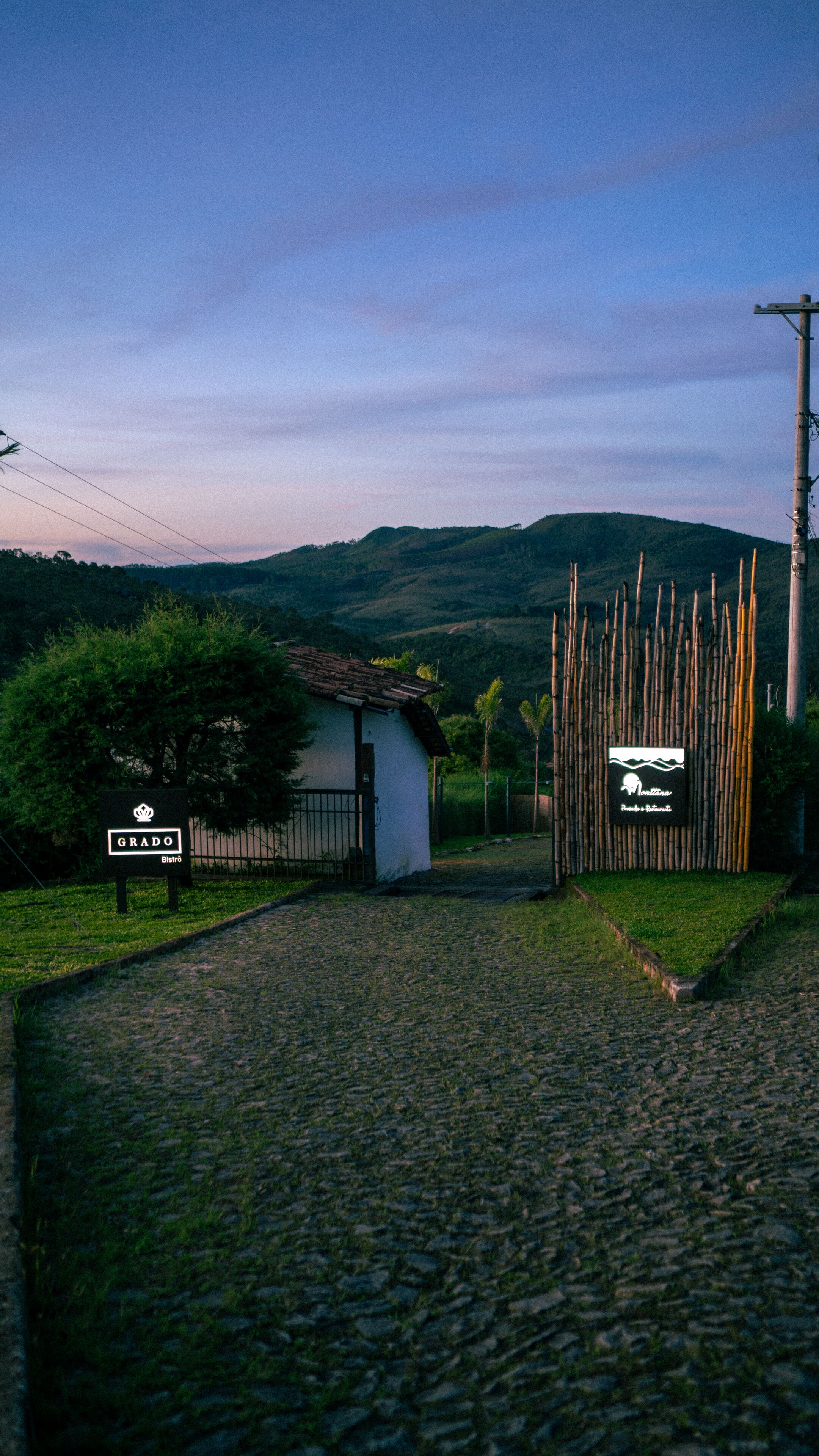 A cobblestone path leading to a white building with a tiled roof, surrounded by bamboo fencing and a sign indicating 'GRADO Bistro'.