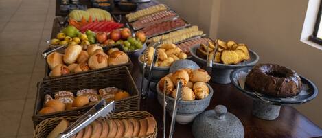 A buffet table with various food items including bread, pastries, fruits, and a chocolate cake.