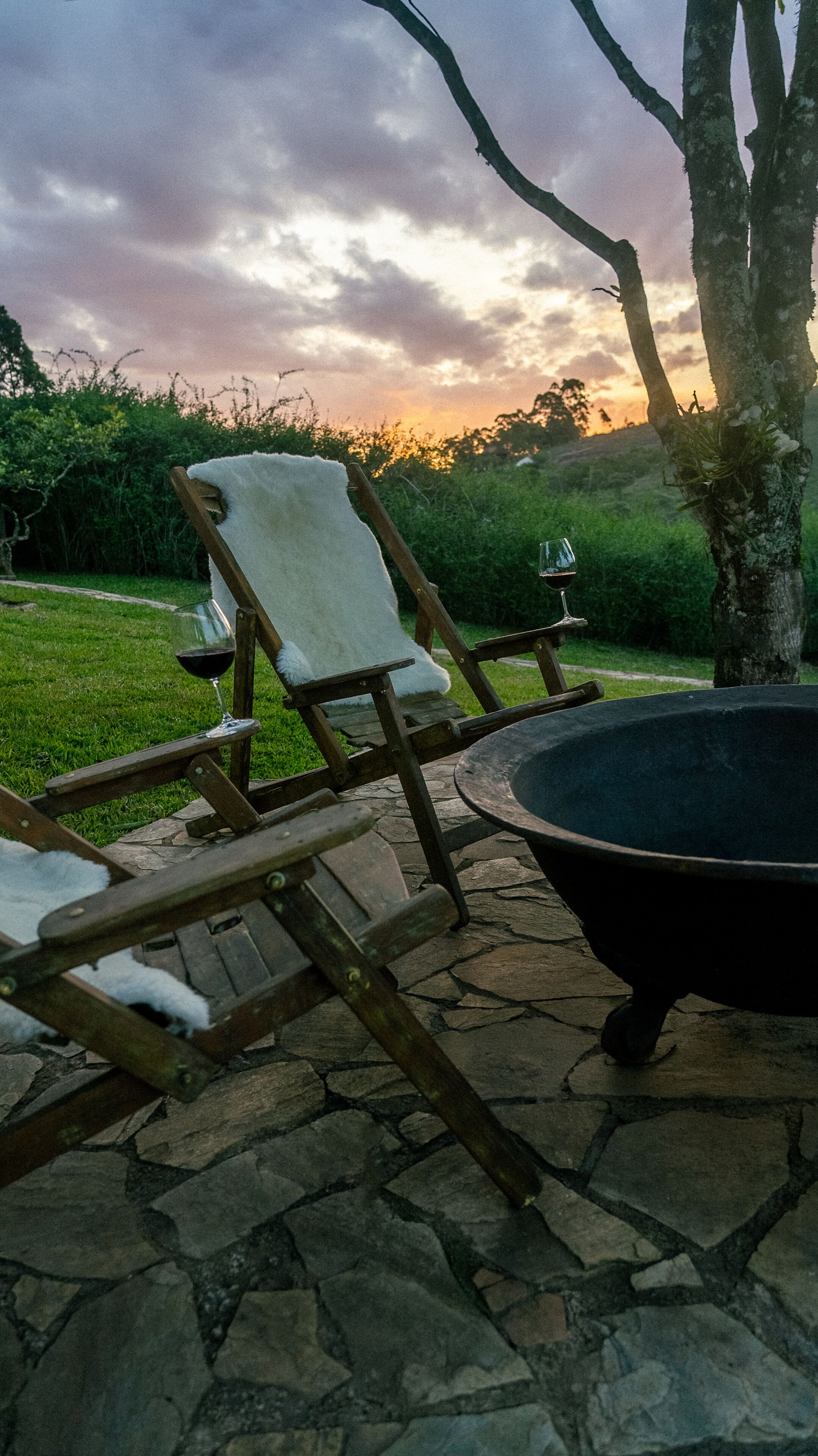 A stone patio with two wooden chairs and a black fire pit.