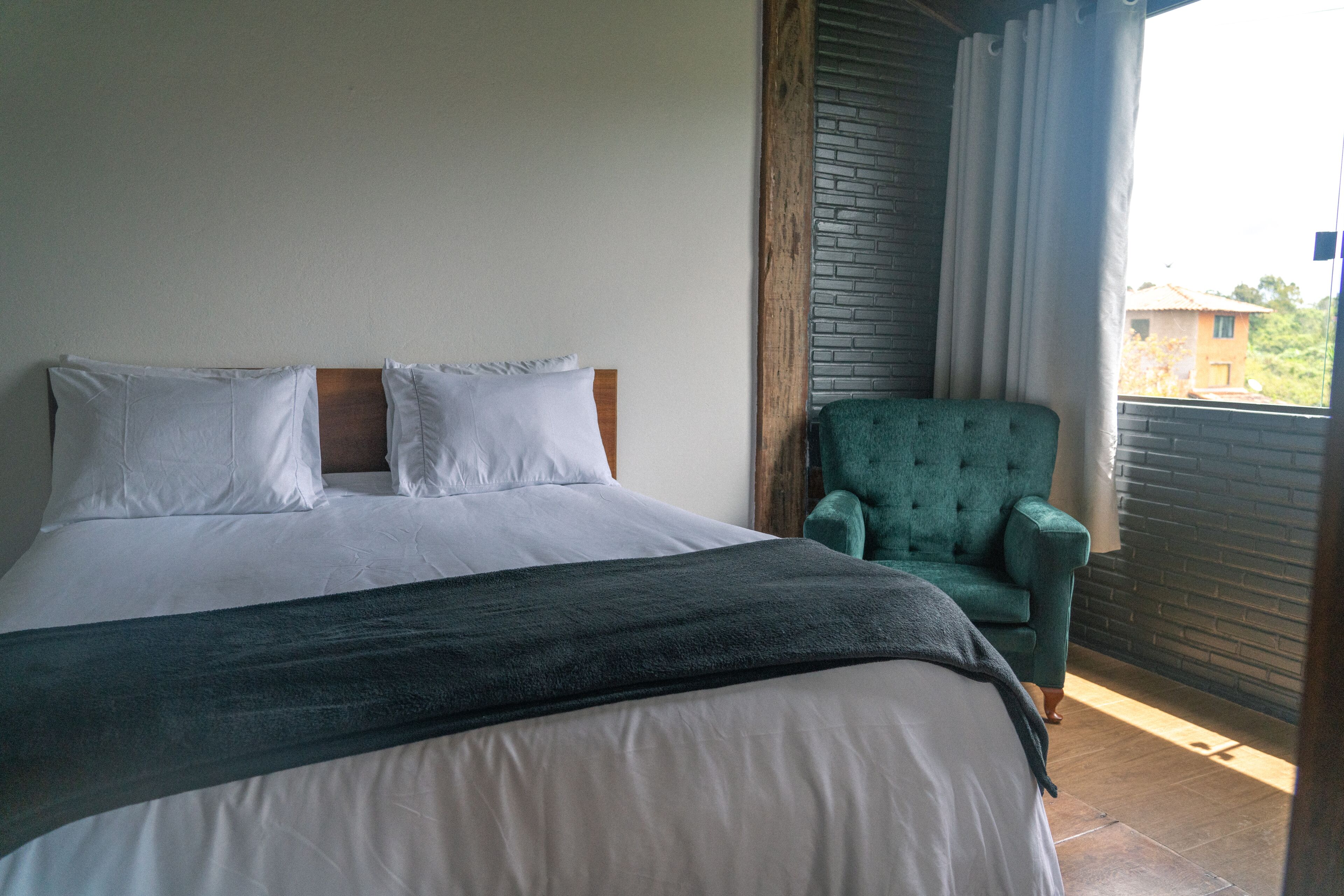 A bedroom with a bed, pillows, a green armchair, and a view of the outside.