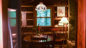 A cozy cabin interior with a wooden dining table, chairs, a hanging light fixture, and a window with a view of trees. - Hikers Retreat in the Linville Gorge Forest (Nebo)