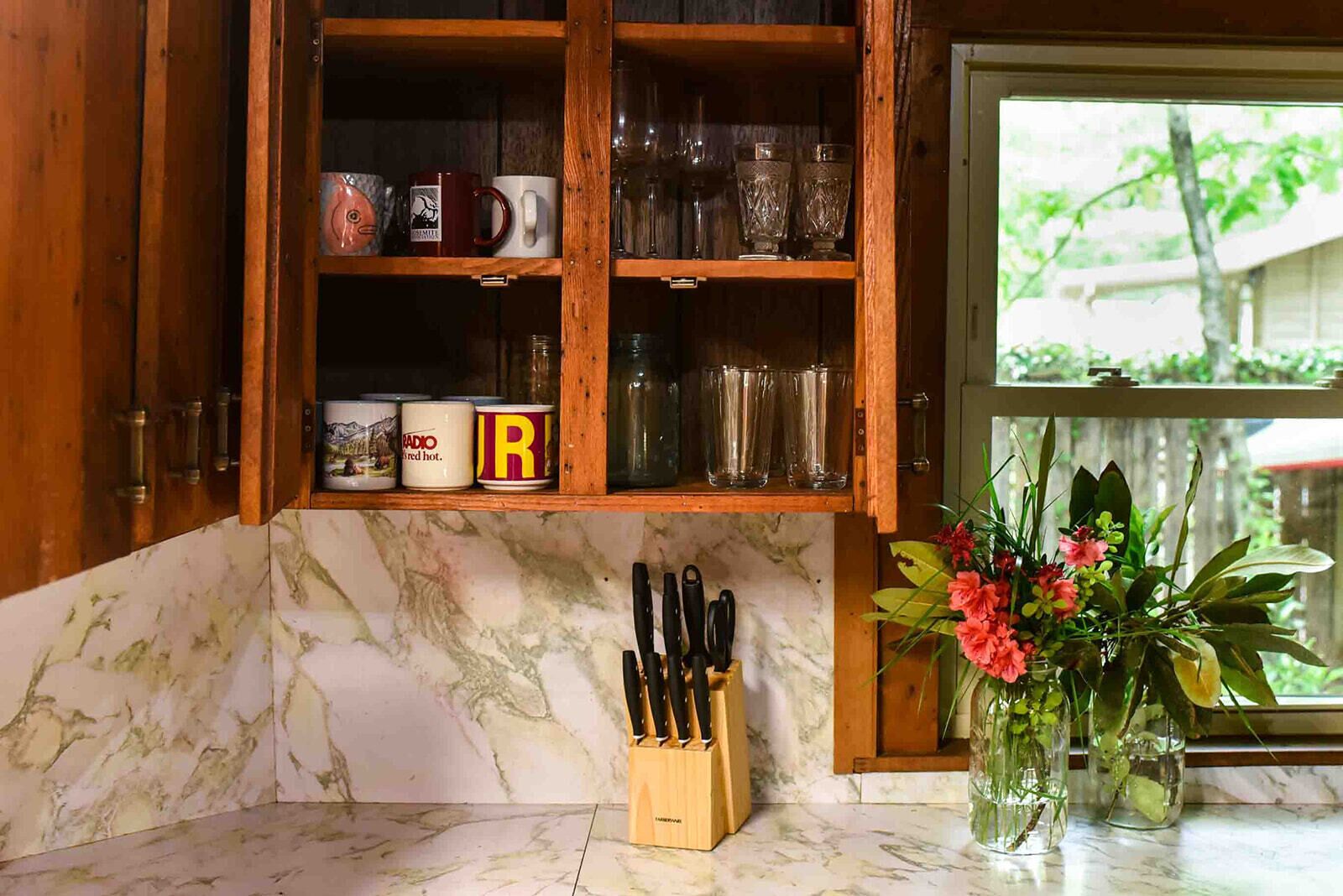 A kitchen with wooden cabinets, a marble countertop, and a window with a view of greenery.