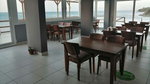 A dining area with tables and chairs, large windows with a view of the sea, and a tiled floor. - Melita Hotel (Urla)