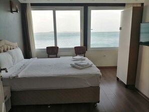 A hotel room with a bed, two chairs, a TV, and a large window overlooking the sea. - Melita Hotel (Urla)