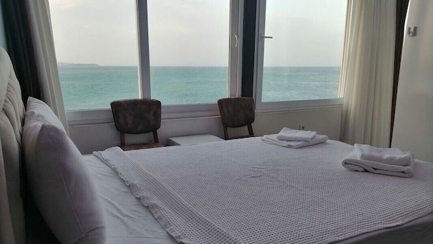 A hotel room with a bed, two chairs, a window with a view of the sea, and a door. - Melita Hotel (Urla)