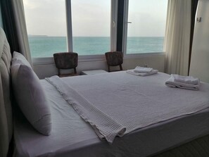 A hotel room with a bed, two chairs, a window with a view of the sea, and a door. - Melita Hotel (Urla)
