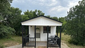 Eine kleine, weiße Holzhütte mit schwarzem Dach und einer Veranda, umgeben von Kies und Grünpflanzen.