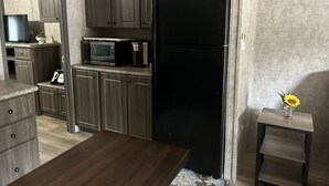 Eine Küche mit dunklen Holdschränken, einem schwarzen Kühlschrank, einer Mikrowelle und einer Kaffeemaschine auf der Arbeitsplatte.