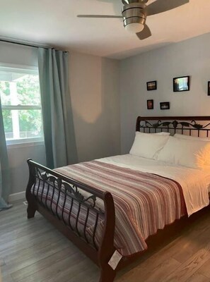 A bedroom with a bed, a ceiling fan, a window with curtains, and framed pictures on the wall. - Relax at Hibiscus Grove - w/ an Amazing Deck View (Kings Mountain)