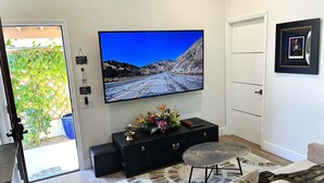 Un salon avec un téléviseur à écran plat fixé au mur, un meuble de rangement noir, une petite table ronde et un canapé beige.
