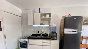 A compact kitchen with white cabinets, a black refrigerator, a stove, and a water dispenser. - Casa duplex na Praia do Francês (Marechal Deodoro)