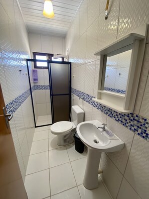 A bathroom with white tiled walls, a shower enclosure, a toilet, and a sink. - Casa duplex na Praia do Francês (Marechal Deodoro)