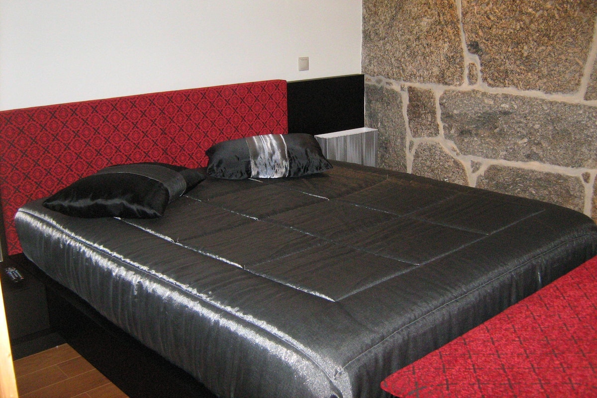A bed with a black and red headboard, a stone wall, and a red and black patterned sofa.