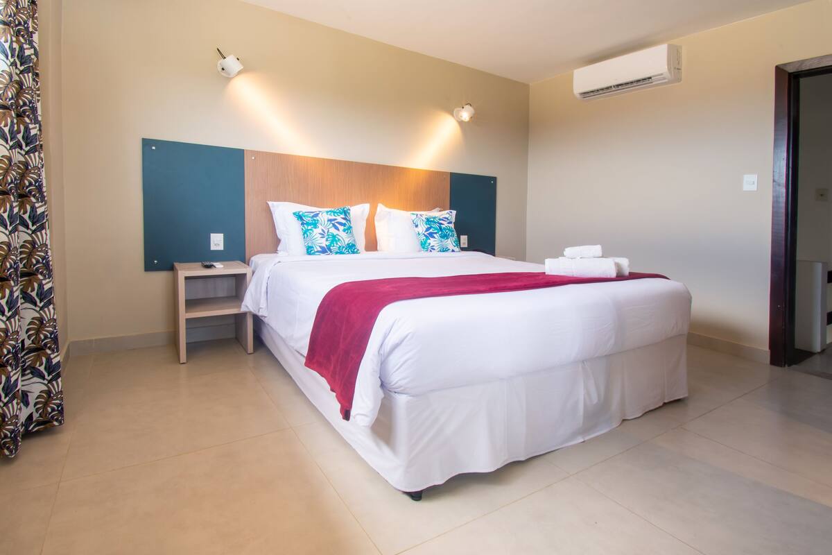 A hotel room with a large bed, a nightstand, an air conditioning unit, and a door.