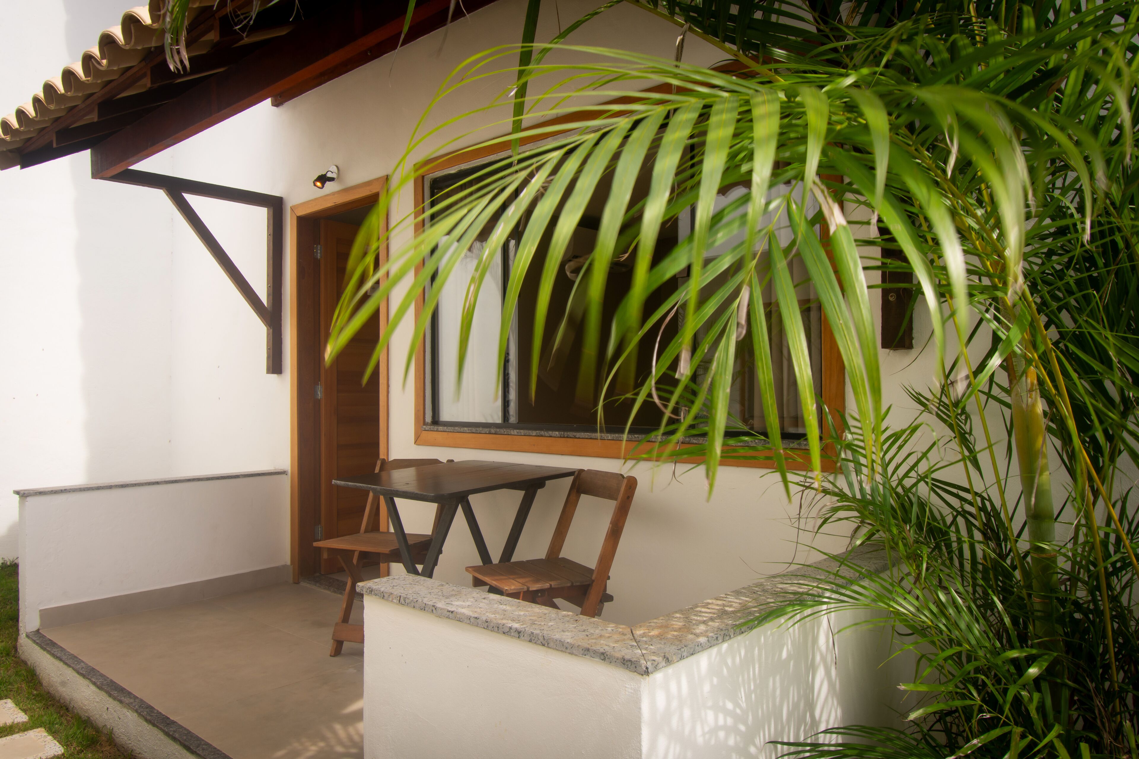Un pequeño patio con una mesa y sillas, una puerta de madera y un ventanal grande.