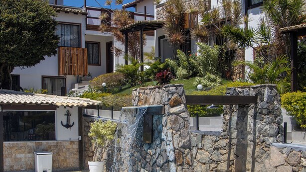 A swimming pool with a stone waterfall feature, surrounded by multi-story buildings with balconies and tropical landscaping. - Gammel Dansk by Latitud Hoteles (Búzios)