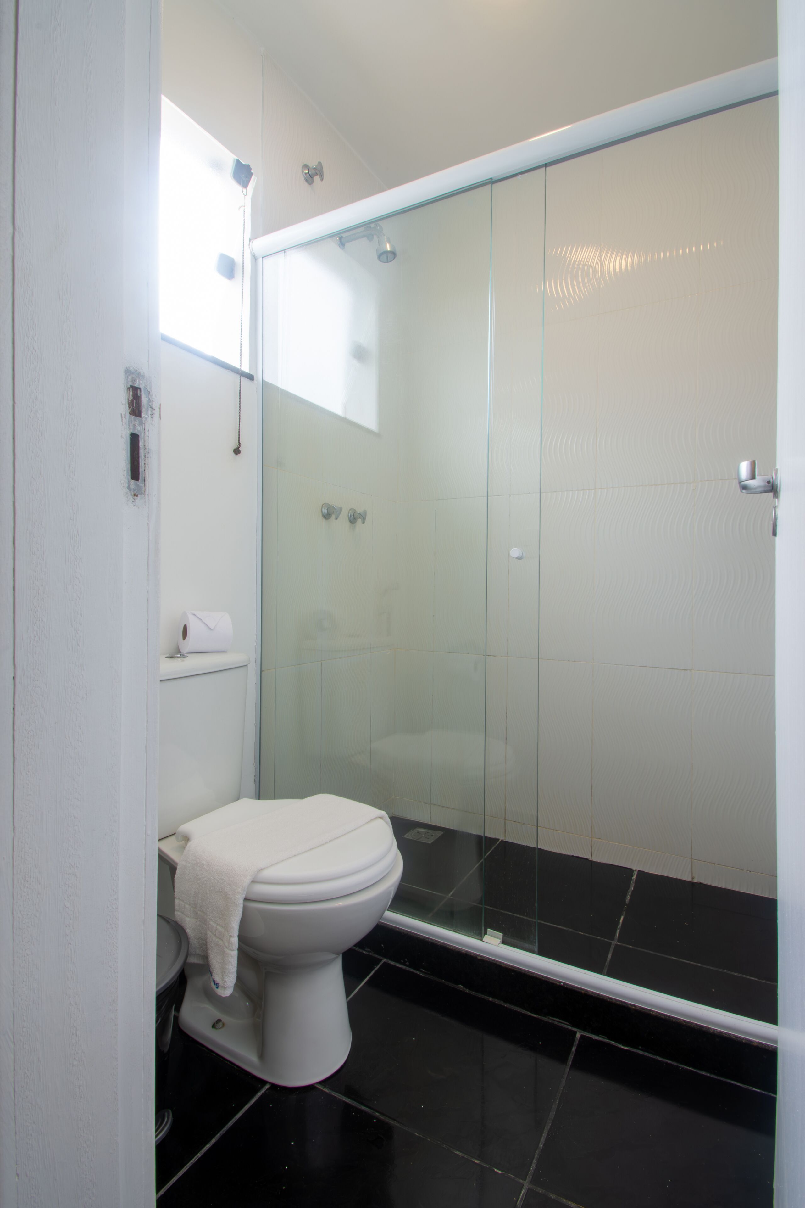 Un baño moderno con ducha de vidrio, inodoro blanco y piso de baldosas negras.