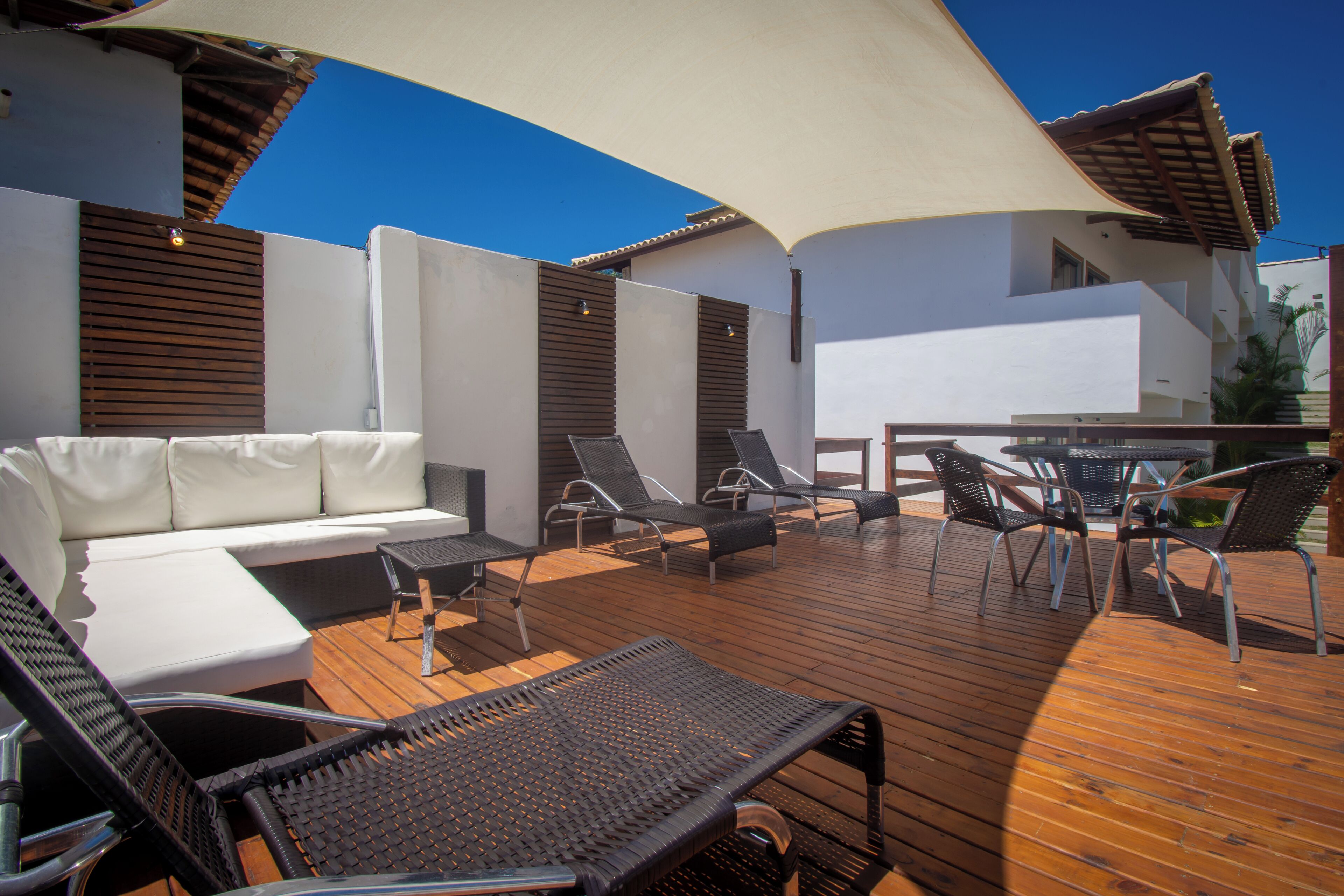 An outdoor deck with a white sofa, black lounge chairs, and a table.