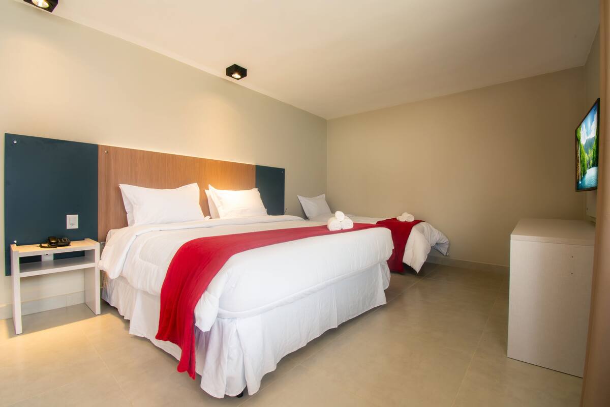 A hotel room with a large bed, a bedside table, a small desk, and a TV mounted on the wall.