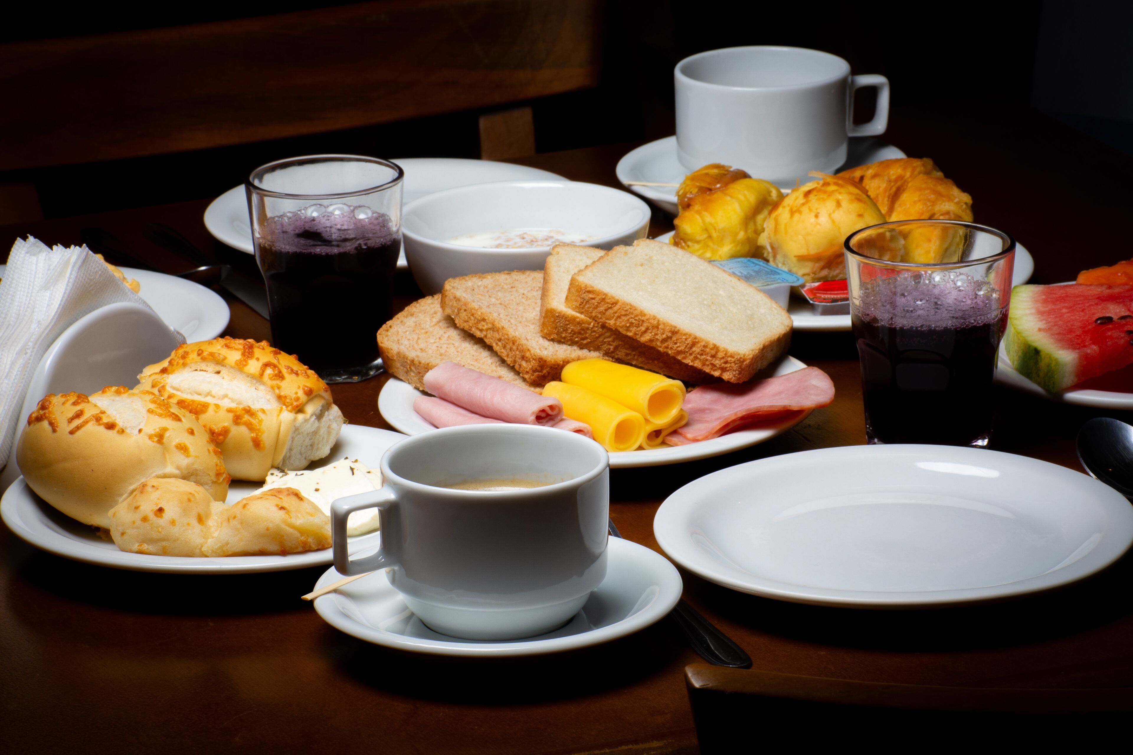 A breakfast table with plates of food, cups, and a bowl.