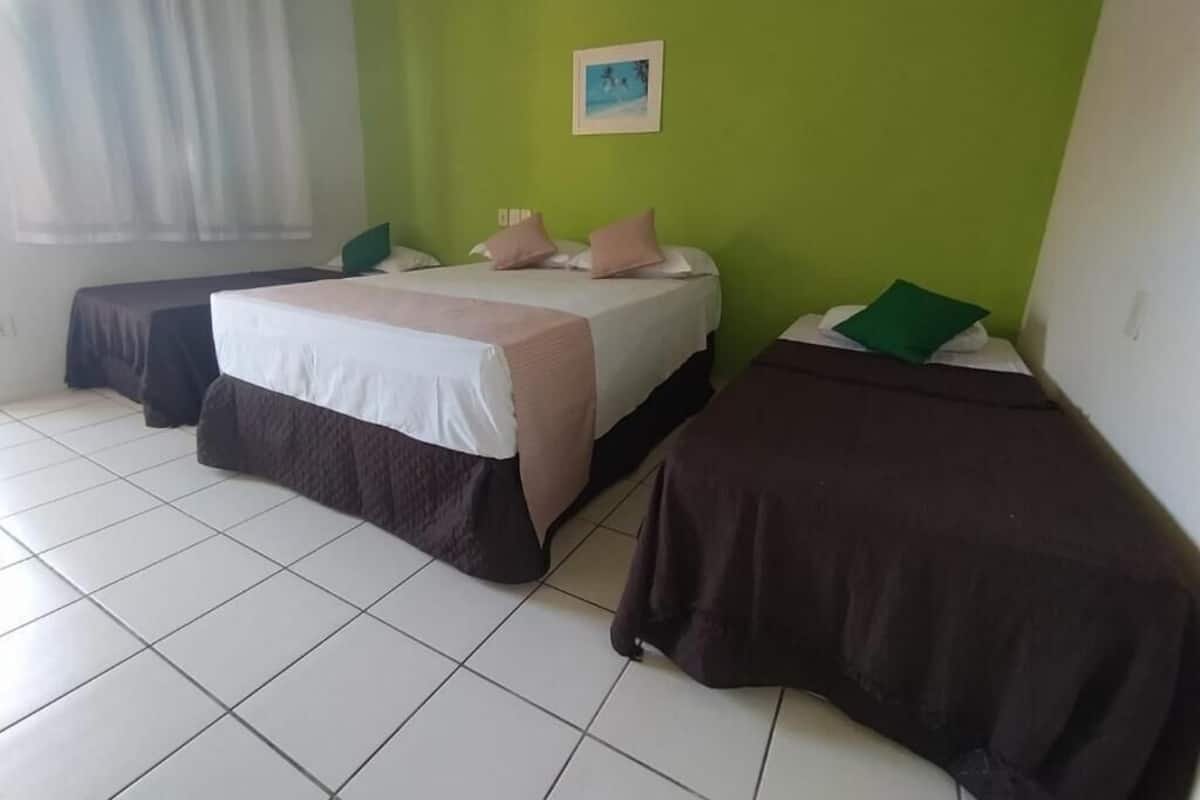 A room with three beds, a green wall, and a picture.