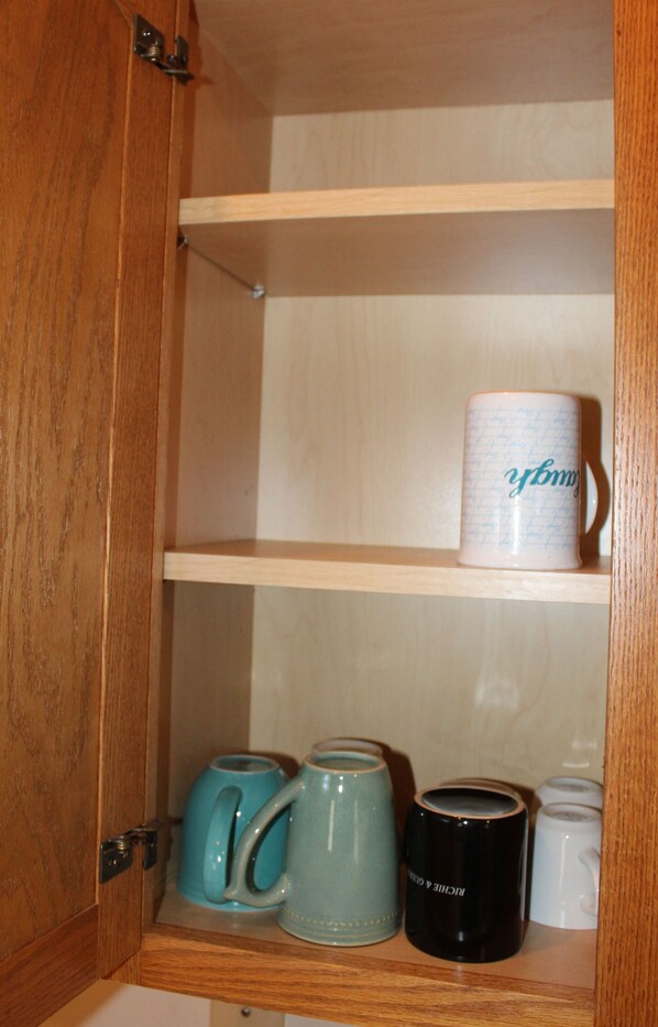 Ein Holzschrank mit Regalen, der verschiedene Tassen und einen Wasserkocher beherbergt.