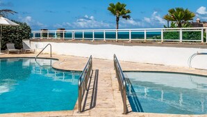 A pool with a white railing, palm trees, and a clear blue sky. - Panoramic Lagoon Studio · Water Backup (San Juan)