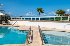 A swimming pool with a white deck, metal railings, and a view of the sea. - Panoramic Lagoon Studio + Resort Pool (San Juan)