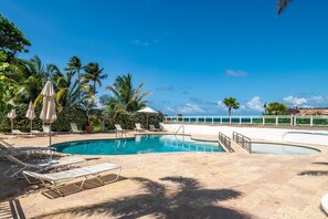 A pool with lounge chairs and umbrellas, surrounded by palm trees and a clear sky. - Panoramic Lagoon Studio + Resort Pool (San Juan)