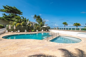 Una piscina con lettini e ombrelloni, circondata da palme e con vista sull'oceano.