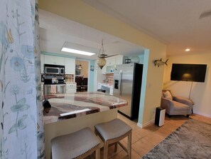A modern kitchen with a central island, a dining area with a chandelier, and a living room with a TV and a sofa.