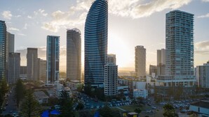 A cityscape with modern high-rise buildings, including a distinctive curved skyscraper, surrounded by a parking area and greenery.
