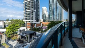 A high-rise building with multiple balconies, a rooftop garden, and a view of other high-rise buildings.