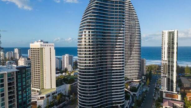 A modern hotel with a curved facade, located in a coastal city with a view of the ocean.