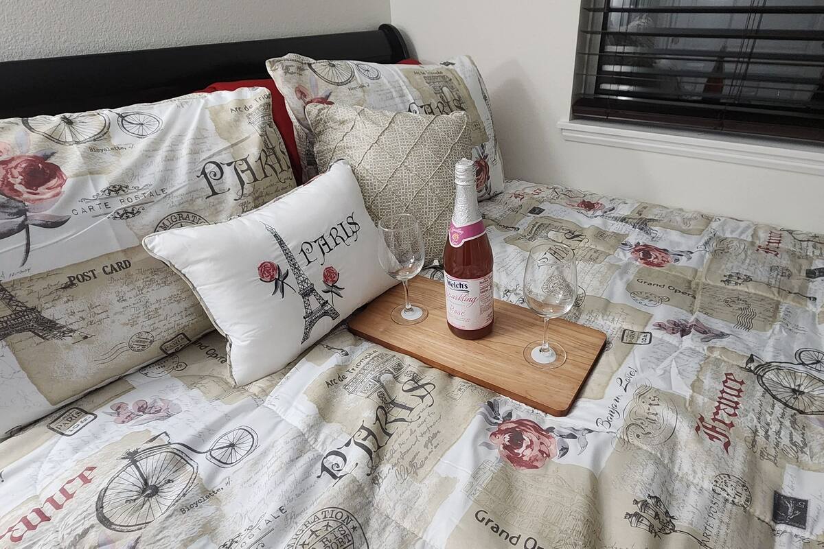 Un lit avec une couette aux motifs parisiens, une bouteille de vin et un verre sur un plateau en bois.