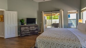 A bedroom with a large bed, a TV on a wooden dresser, and a sliding glass door leading to an outdoor patio.