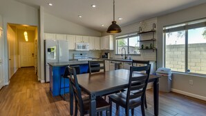 A modern kitchen with white cabinets, a blue island, and a dining area with dark wooden furniture.