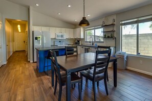 Een moderne keuken met witte kasten, een blauw eiland en een eethoek met donker houten meubilair.