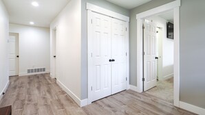 A hallway with a wooden floor, white walls, and a white door with a vent.