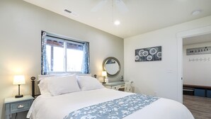A neatly arranged bedroom with a bed, bedside tables, a window with curtains, a mirror, and wall art.