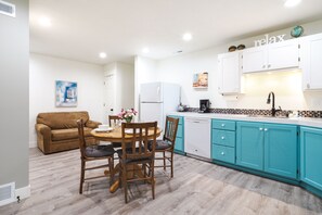 A modern kitchen with teal cabinets, a white refrigerator, and a dining area with wooden chairs and a table.