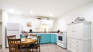A kitchen with teal cabinets, a white refrigerator, and a wooden dining table with chairs.