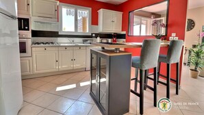 Una cocina con armarios blancos, encimera negra y una pequeña barra con dos sillas.