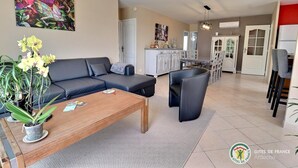 Una sala de estar moderna con un sofá, una mesa de centro y sillas. En el fondo, se ve una zona de cocina con una mesa de comedor y sillas.