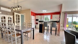 Una cocina moderna con armarios blancos, una mesa de comedor con sillas y vistas al exterior a través de amplios ventanales.