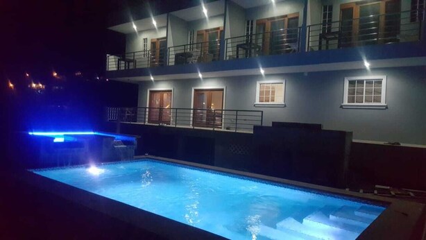 A swimming pool with a blue light, a multi-story building with balconies, and a night-time setting. - Beausejour Vista Studio1 (Gros Islet)